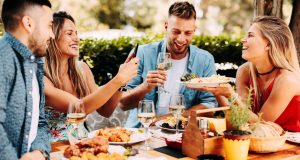 Deux couples d'amis jeunes et souriants attablés en restaurant terrasse, autour d'un copieux repas et de verres de vin.